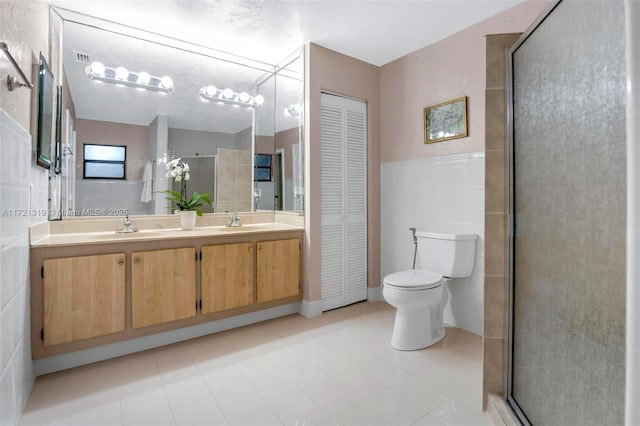 bathroom featuring vanity, toilet, a shower with shower door, and tile walls