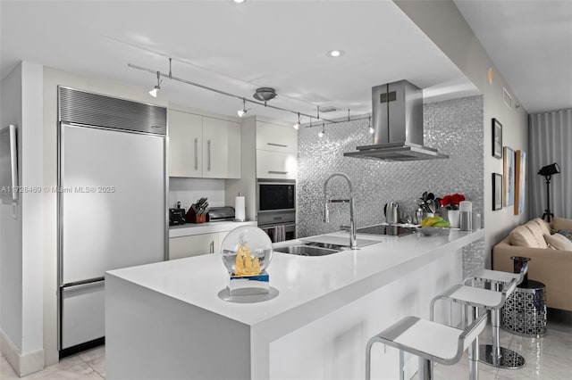 kitchen featuring a kitchen bar, sink, white cabinetry, built in refrigerator, and ventilation hood