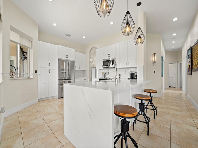 kitchen with stainless steel appliances, decorative light fixtures, light tile patterned flooring, white cabinets, and a breakfast bar