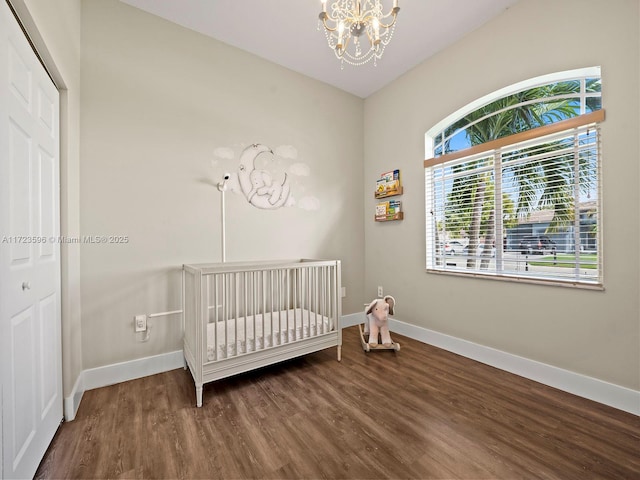 bedroom featuring a nursery area, an inviting chandelier, a closet, and hardwood / wood-style floors