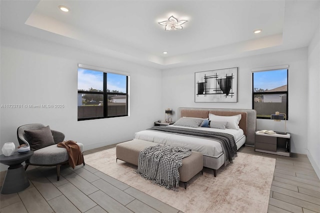 bedroom with a tray ceiling, multiple windows, and light wood-type flooring