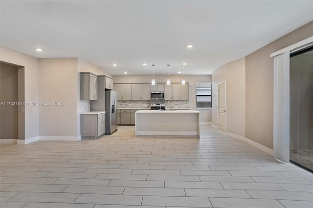 kitchen featuring tasteful backsplash, hanging light fixtures, gray cabinets, stainless steel appliances, and a kitchen island with sink