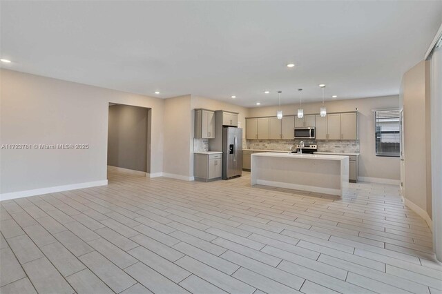 kitchen featuring gray cabinets, appliances with stainless steel finishes, decorative light fixtures, backsplash, and a kitchen island with sink