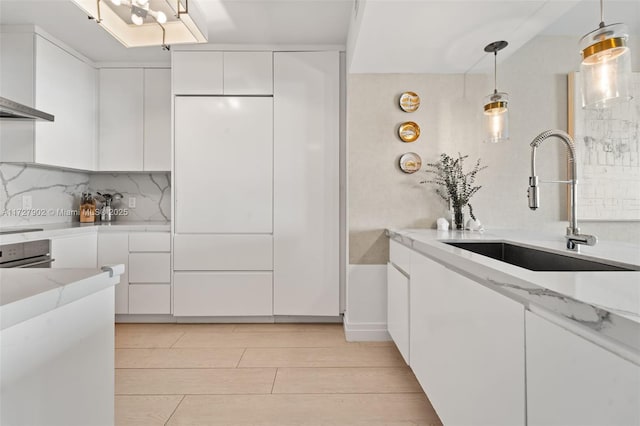 kitchen with decorative light fixtures, white cabinetry, sink, oven, and backsplash