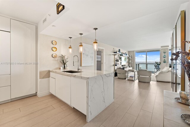 kitchen with sink, a water view, light stone countertops, white cabinets, and kitchen peninsula