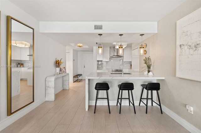 kitchen featuring a kitchen bar, wall chimney exhaust hood, white cabinetry, hanging light fixtures, and kitchen peninsula