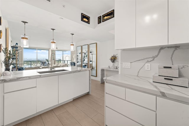 kitchen with pendant lighting, sink, white cabinetry, backsplash, and light stone counters