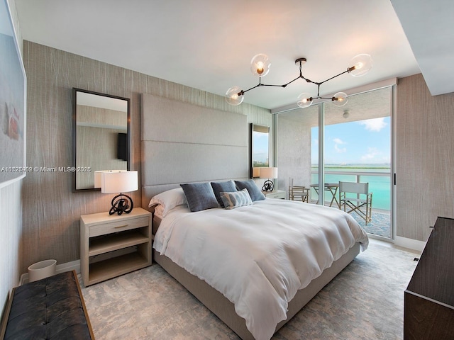 bedroom with a water view, expansive windows, an inviting chandelier, and access to outside