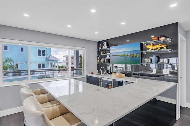 bar with light stone counters, sink, and dark hardwood / wood-style floors