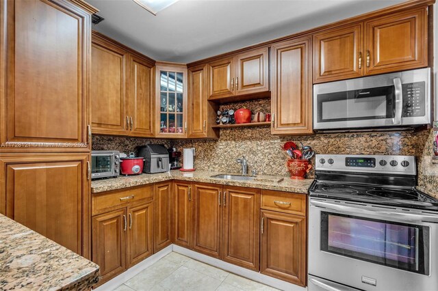 kitchen with decorative backsplash, light stone countertops, appliances with stainless steel finishes, and sink