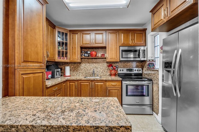 kitchen with light stone countertops, stainless steel appliances, tasteful backsplash, sink, and light tile patterned floors