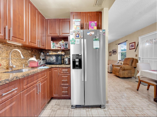 kitchen with light stone countertops, a textured ceiling, sink, backsplash, and stainless steel fridge