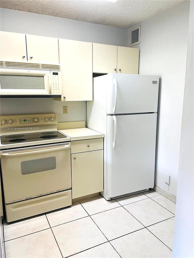 kitchen with light tile patterned floors, white appliances, a textured ceiling, and cream cabinets