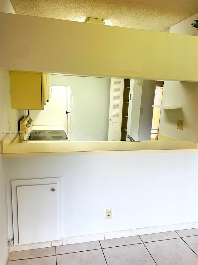 kitchen featuring light tile patterned floors, range, kitchen peninsula, and white fridge