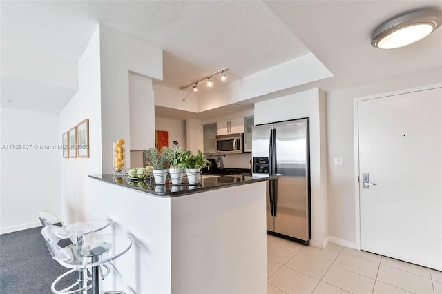 kitchen with light tile patterned floors, appliances with stainless steel finishes, white cabinets, and kitchen peninsula