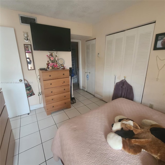 bedroom with multiple closets, light tile patterned floors, and a textured ceiling