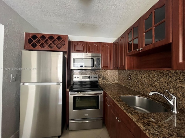 kitchen with appliances with stainless steel finishes, backsplash, dark stone countertops, a textured ceiling, and sink