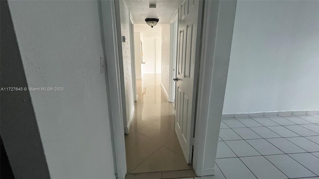 hallway with a textured ceiling and light tile patterned flooring