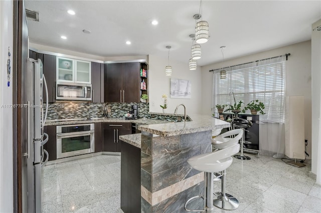 kitchen featuring kitchen peninsula, appliances with stainless steel finishes, hanging light fixtures, light stone counters, and a breakfast bar