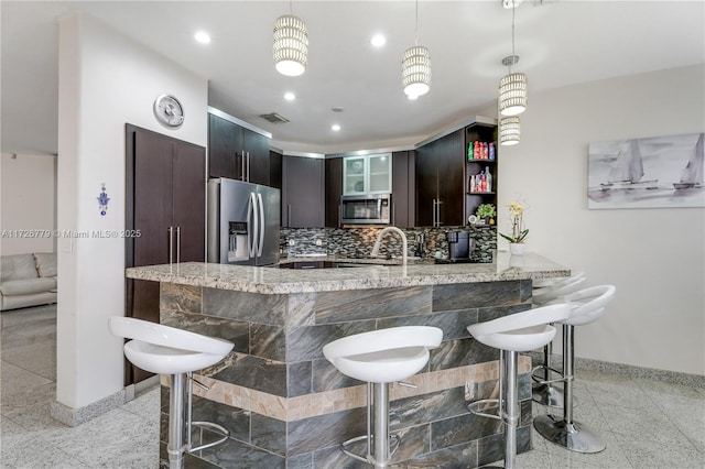 kitchen featuring pendant lighting, kitchen peninsula, a kitchen bar, stainless steel appliances, and dark brown cabinets