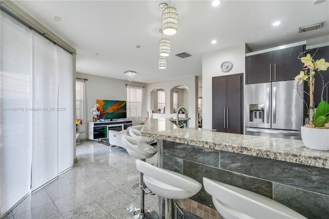 kitchen with dark brown cabinets, sink, light stone countertops, a kitchen breakfast bar, and stainless steel fridge