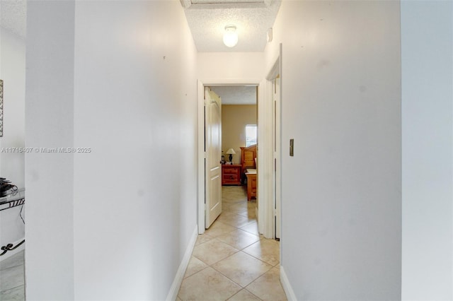 hallway featuring a textured ceiling, baseboards, and light tile patterned floors