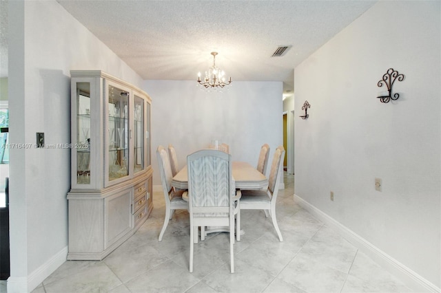 dining area with a textured ceiling, baseboards, visible vents, and an inviting chandelier