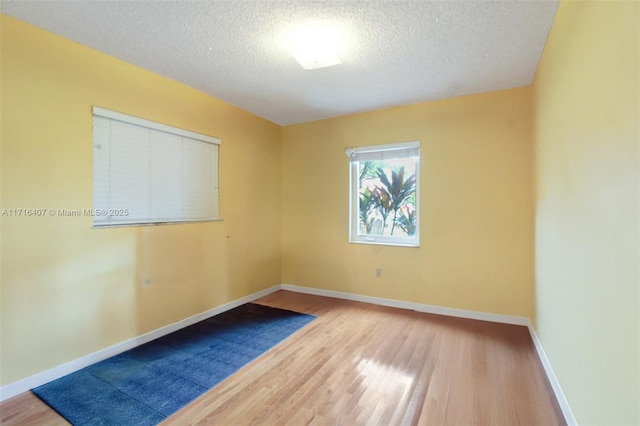 unfurnished room with a textured ceiling, baseboards, and wood finished floors