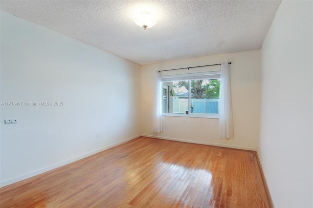 unfurnished room with light wood-style floors, baseboards, and a textured ceiling