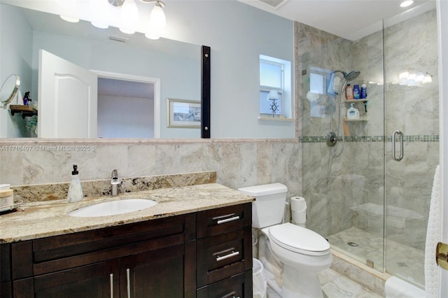 bathroom with a wainscoted wall, tile walls, toilet, a shower stall, and vanity