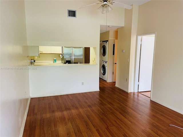 interior space with ceiling fan, dark hardwood / wood-style floors, high vaulted ceiling, and stacked washer and dryer