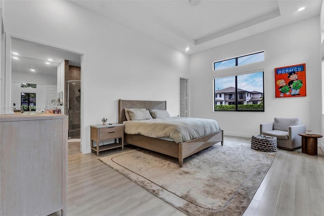 bedroom featuring baseboards, a raised ceiling, ensuite bathroom, light wood-type flooring, and recessed lighting