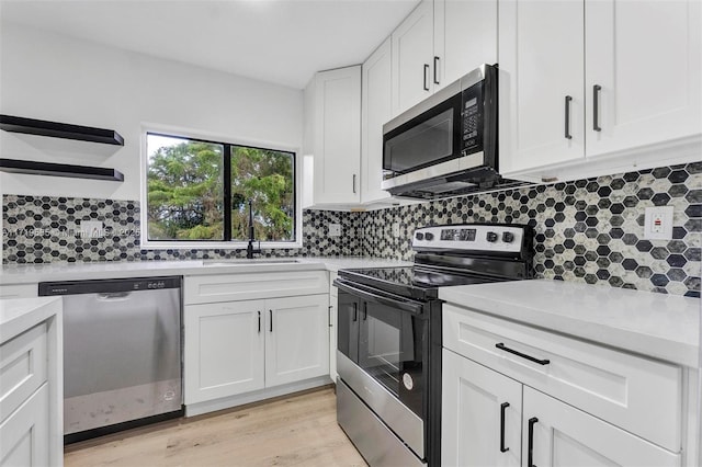 kitchen featuring white cabinetry, stainless steel appliances, light hardwood / wood-style floors, sink, and backsplash