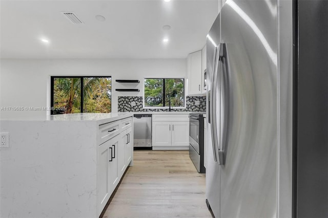 kitchen featuring light stone countertops, white cabinets, appliances with stainless steel finishes, tasteful backsplash, and light hardwood / wood-style floors