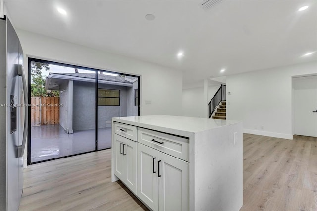 kitchen with light wood-type flooring, white cabinetry, stainless steel fridge, and a kitchen island