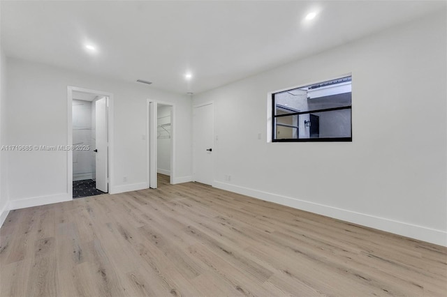 unfurnished bedroom with a walk in closet, a closet, connected bathroom, and light hardwood / wood-style floors