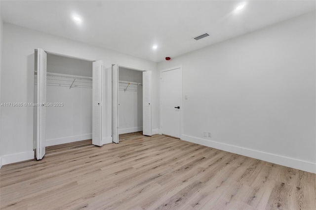 unfurnished bedroom featuring two closets and light hardwood / wood-style flooring