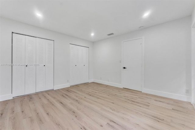 unfurnished bedroom featuring light wood-type flooring and multiple closets