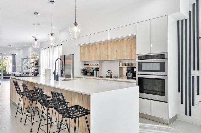 kitchen with an island with sink, a breakfast bar area, stainless steel appliances, decorative light fixtures, and white cabinets