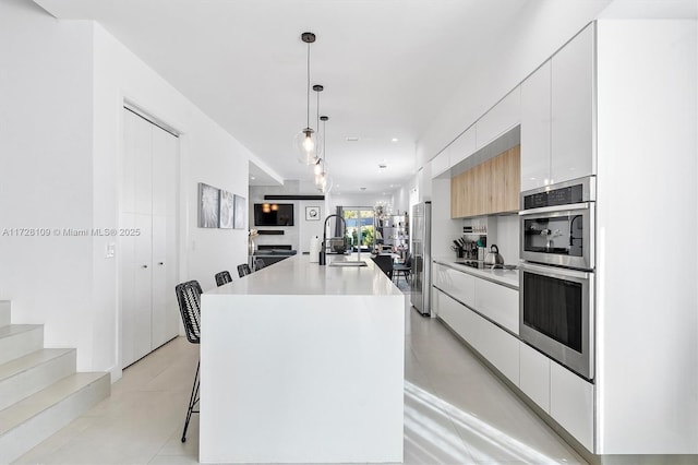 kitchen with pendant lighting, white cabinetry, an island with sink, sink, and a breakfast bar