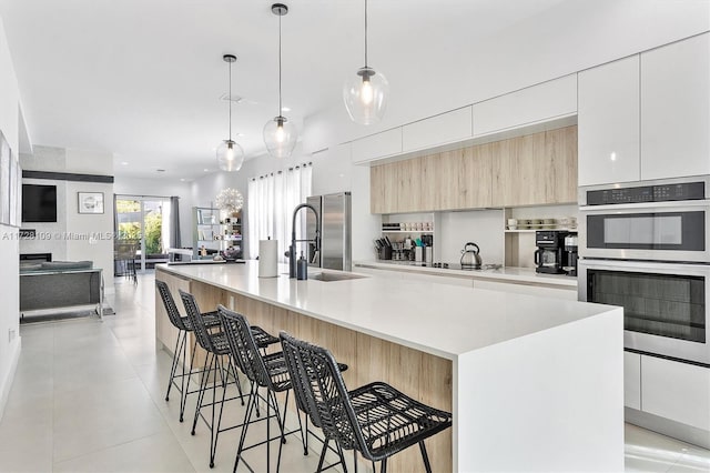 kitchen with a spacious island, a breakfast bar, sink, stainless steel appliances, and white cabinets