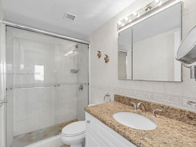 bathroom featuring tile walls, vanity, a shower with shower door, and toilet