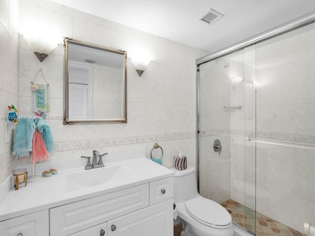 bathroom with tile walls, vanity, a shower with shower door, and toilet