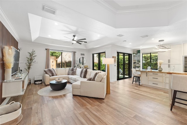 living room with crown molding, a healthy amount of sunlight, light hardwood / wood-style flooring, and a raised ceiling