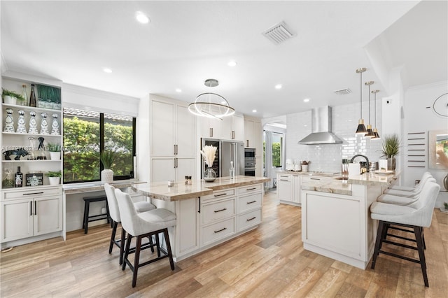 kitchen with hanging light fixtures, wall chimney range hood, a breakfast bar area, and an island with sink