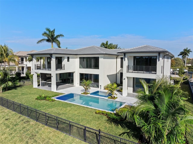 rear view of house with a pool with hot tub, a yard, a balcony, and a patio