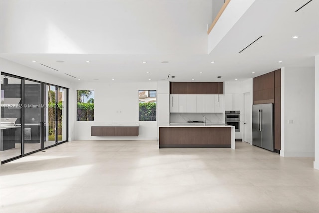 kitchen with appliances with stainless steel finishes, dark brown cabinetry, an island with sink, sink, and backsplash