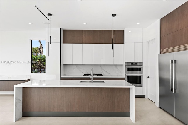 kitchen featuring sink, hanging light fixtures, stainless steel appliances, and an island with sink