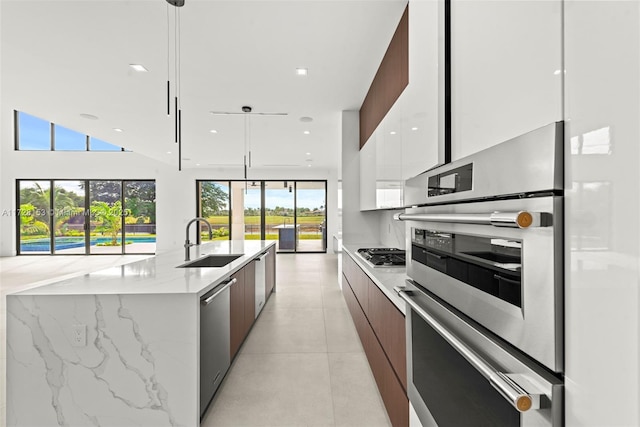 kitchen with white cabinets, appliances with stainless steel finishes, sink, hanging light fixtures, and a kitchen island with sink