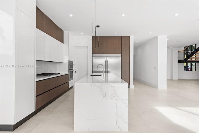 kitchen featuring hanging light fixtures, white cabinets, appliances with stainless steel finishes, and a center island with sink